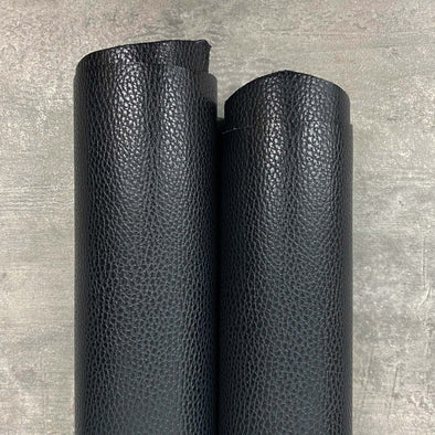 Two Rolls of deep, rich, glossy black leather with a pebble grain print sits on a concrete background